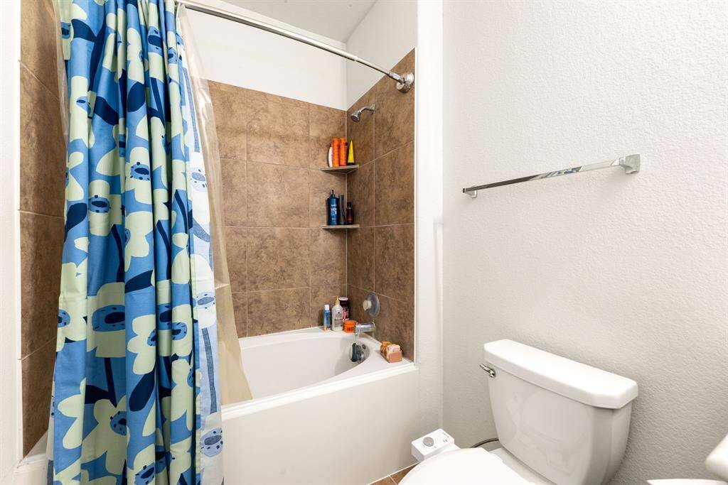 Secondary bathroom features light countertops and dark cabinets, custom paint, shower/tub combo with tile surround, large mirror, tile floors, sleek fixtures and modern finishes, plenty of space to accommodate any visiting family or guests.