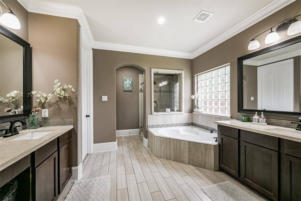 Primary En-Suite Bath Features Dual Vanities, Walk-In Shower, Soaking Tub, Framed Mirrors and a Walk-In Closet