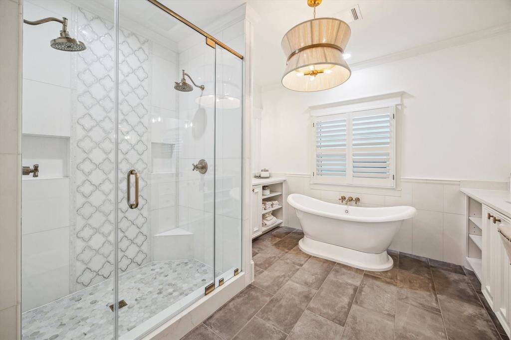 The glamorous ensuite bath, remodeled in 2023, boasts a glass-enclosed shower with double showerheads, a freestanding soaking tub, and double sinks with separate vanities.