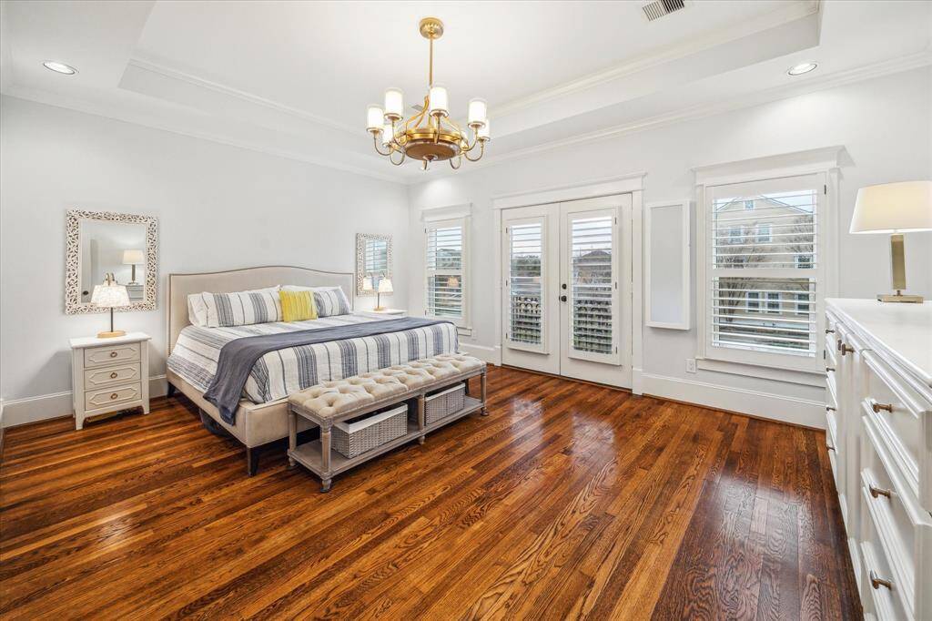 Step into the luxurious primary suite featuring a coffered ceiling, a stylish ceiling fan with lighting, hardwood floors, plantation shutters, a built-in dresser, and a charming Juliet balcony. The expansive walk-in closet with built-ins will make all your organizational dreams come true!