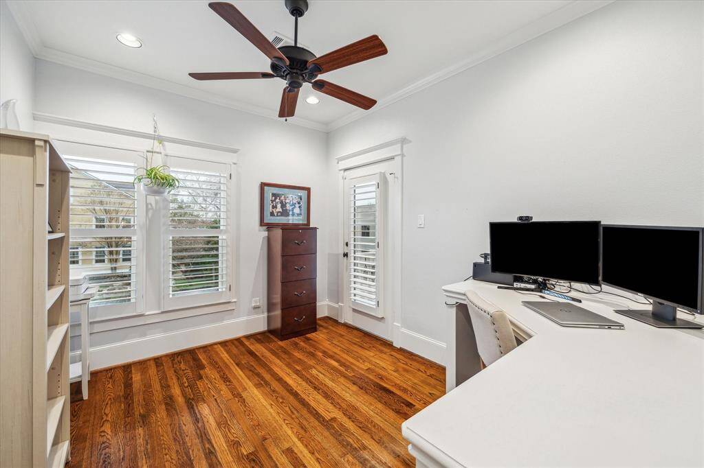Home office with a built-in desk, porch access, hardwood floors, ceiling fan and plantation shutters.