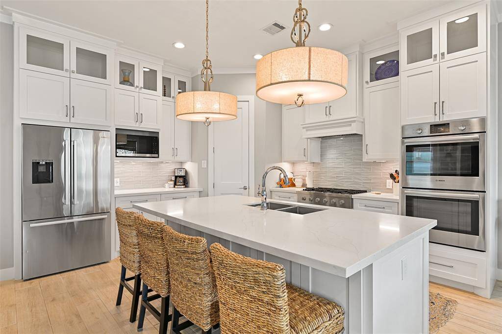 This gourmet kitchen is a chef’s dream with high-end stainless steel BOSCH appliance package, quartz countertops, and custom cabinetry- notice the beautiful detail on the backsplash tile that mimics waves.  The lighting pendant selection is an excellent addition to this beach home.