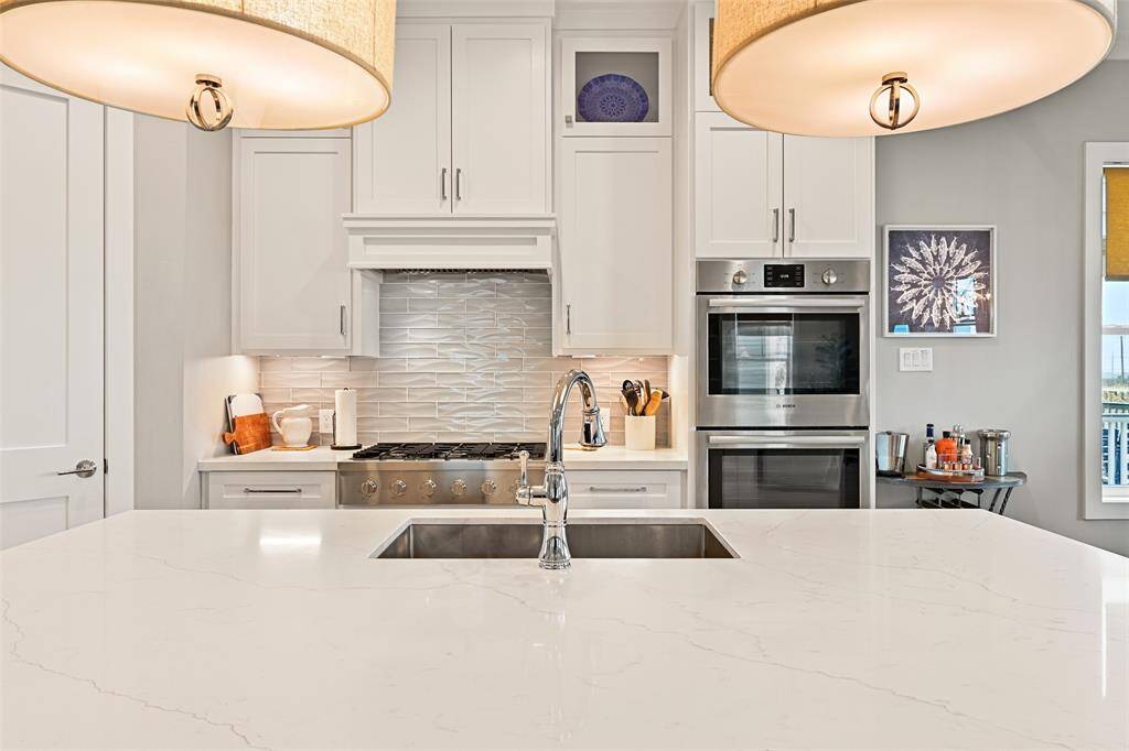 Beautiful quartz countertops, lighted cabinetry,  BOSCH stainless-steel appliances and custom finishes bring functionality and luxury together in this chef's kitchen.  Notice the textured tile backsplash that mimics the waves of the Gulf.