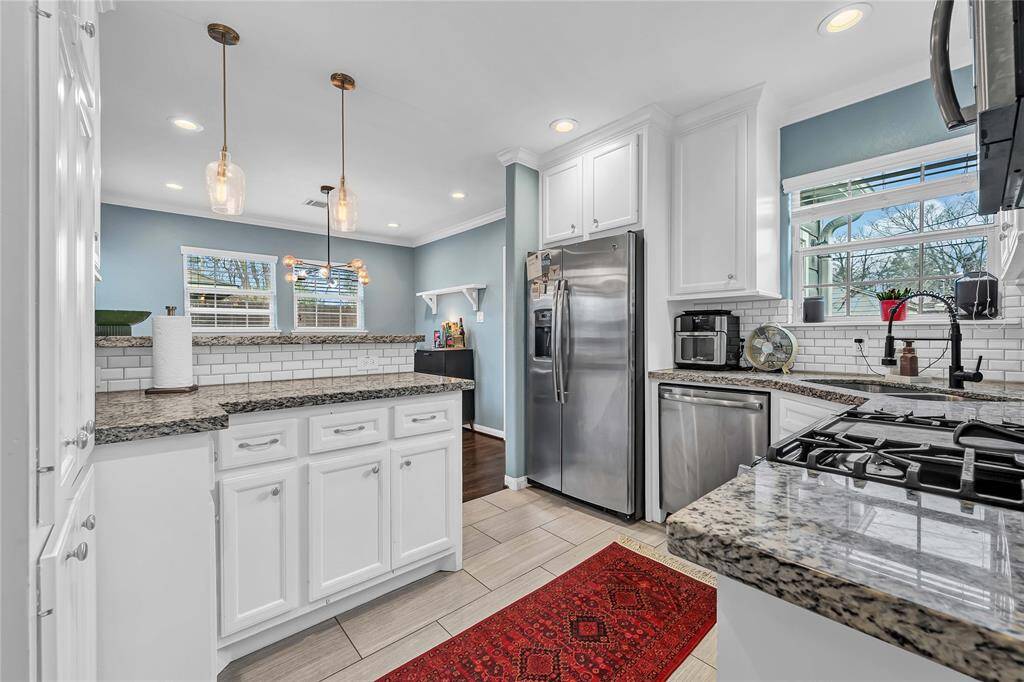 The kitchen includes stainless steel appliances, pendant lighting, and ample natural light from multiple windows.