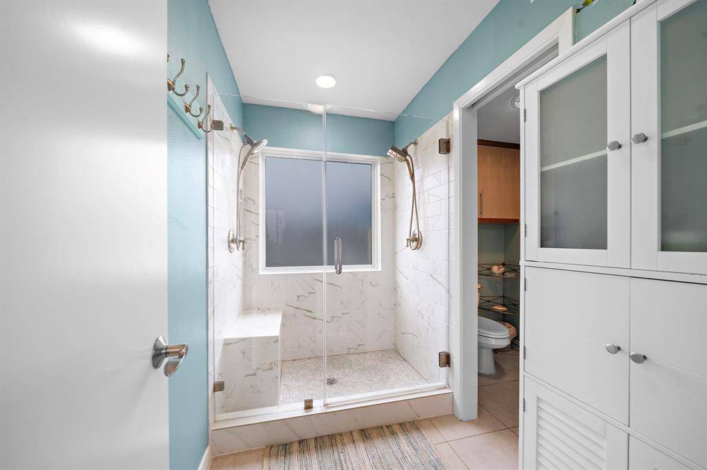 Primary bathroom with frameless glass tiled shower with dual shower heads.  Separate water closet with storage.