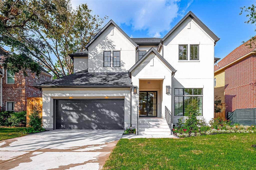 This photo showcases a modern two-story home with a sleek white exterior and dark roof. It features a large driveway leading to a double garage. The front entrance is inviting, with steps and landscaped greenery, surrounded by mature trees.
