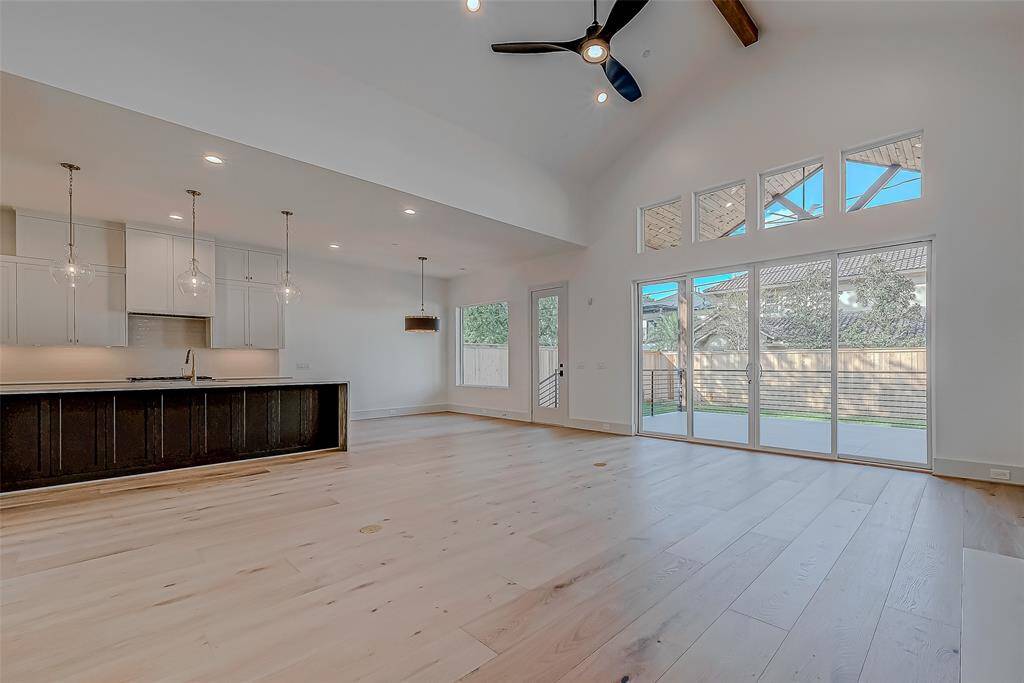 This spacious open-concept living area features high ceilings, abundant natural light through large windows, and modern finishes. The kitchen boasts a sleek island with pendant lighting, and the room opens to a private backyard, perfect for entertaining.