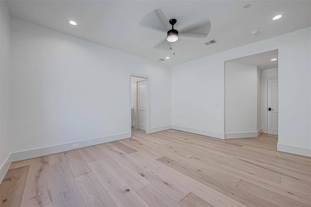 This is a spacious, bright room with light wood flooring, white walls, and a ceiling fan. Recessed lighting and a modern design add to its appeal, with two doorways leading to other areas of the home.