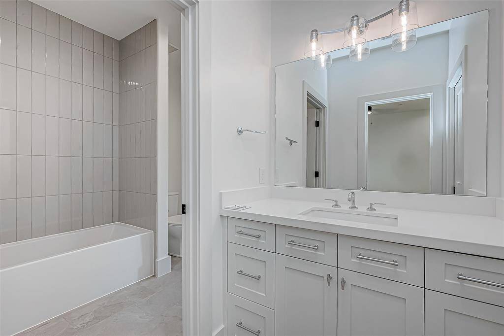 This modern bathroom features a sleek vanity with ample storage, a large mirror with stylish lighting, and a bathtub with contemporary tile work. The neutral color palette enhances the clean, spacious feel.