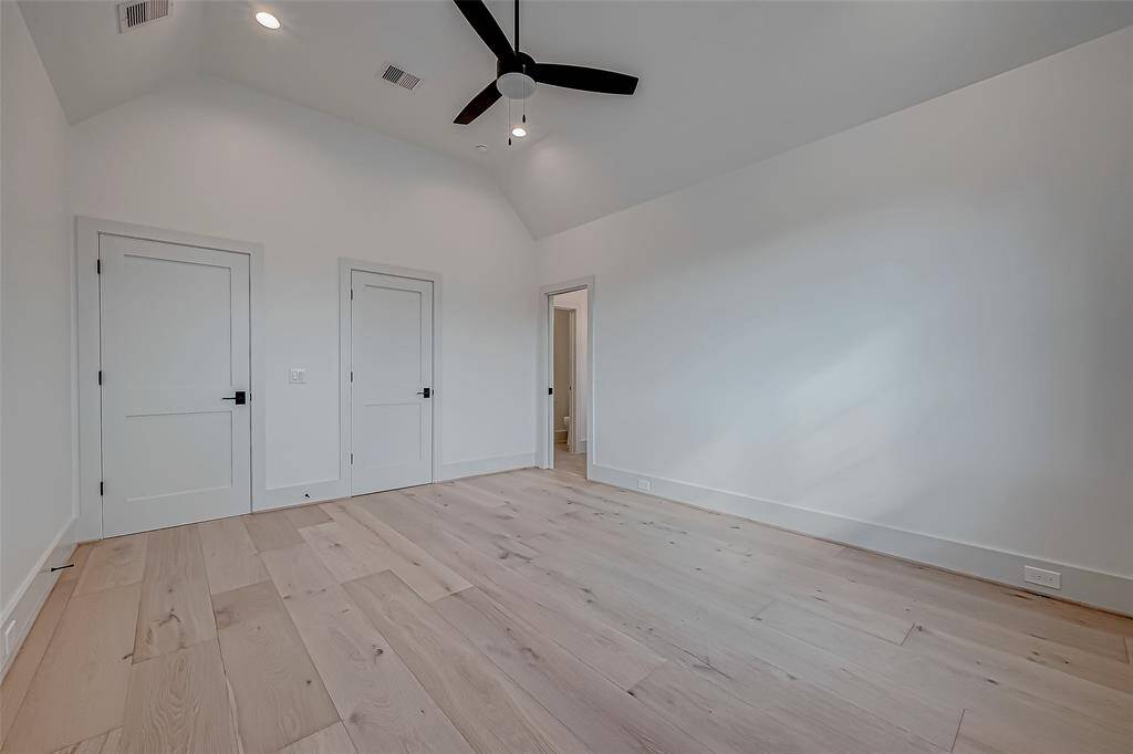 This photo shows a spacious room with high ceilings, light wood flooring, and neutral walls. It features a modern ceiling fan and multiple doors, ideal for a bedroom or office space. Natural light enhances the airy atmosphere.