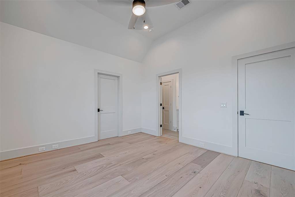 This photo shows a bright, spacious room with light wood flooring and white walls. It features three doors and a ceiling fan, creating a clean, modern feel. Ideal for a bedroom or home office.