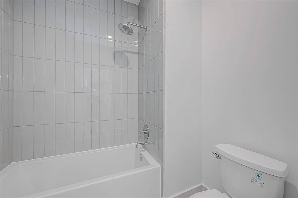 This bathroom features a modern design with a sleek bathtub and shower combination. The walls are adorned with vertical tiles, and the space is complemented by a clean, white toilet.
