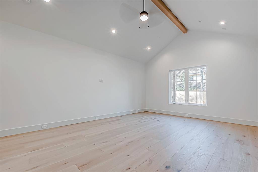This spacious room features high ceilings with a wooden beam, modern lighting, and large windows that allow natural light to flood in. The light wood flooring complements the neutral walls, creating a bright and airy atmosphere.