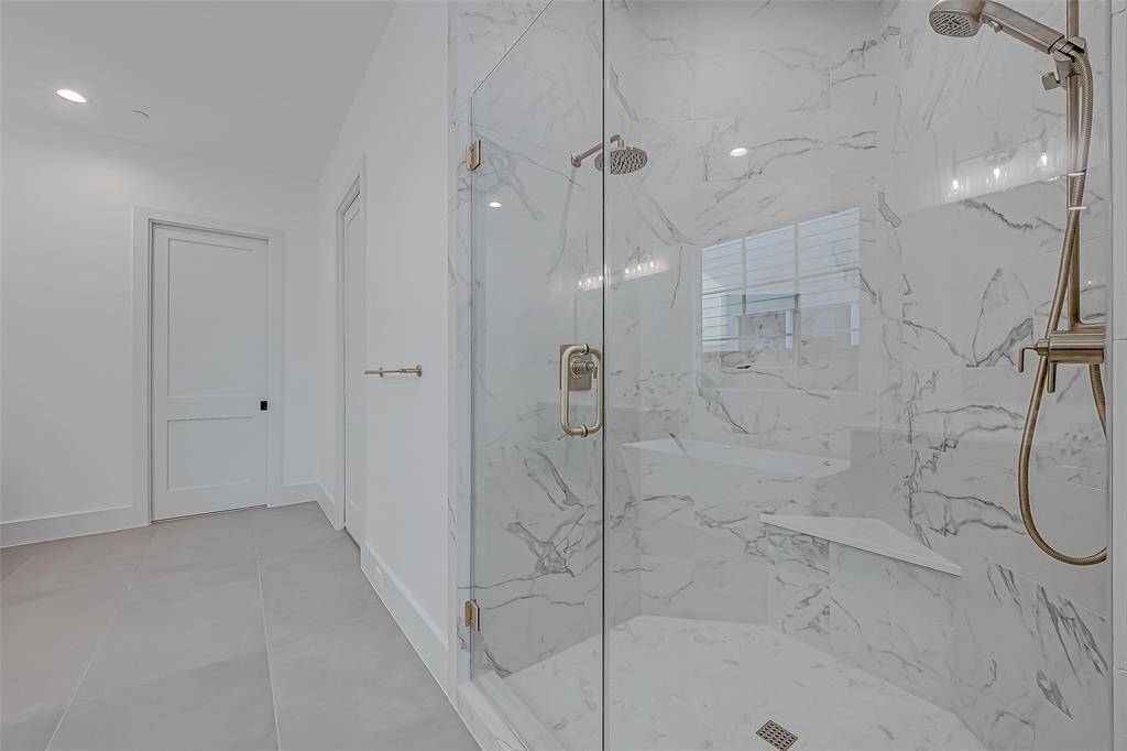 This photo showcases a modern bathroom with a spacious glass-enclosed shower featuring elegant marble tile and dual shower heads. The space is bright with neutral tones, a sleek design, and ample room for comfort.