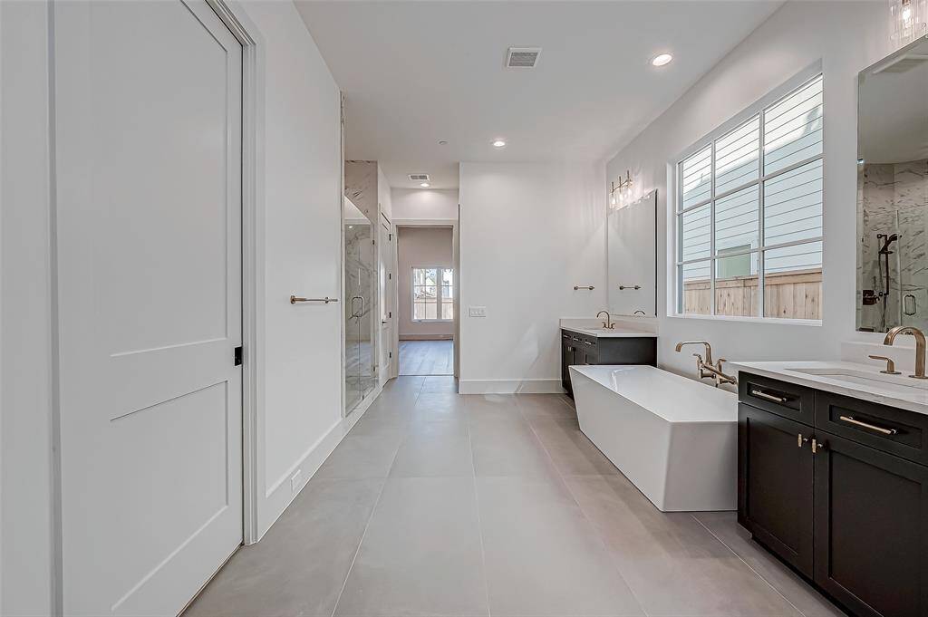 This spacious bathroom features a modern design with a freestanding tub, dual sinks with sleek countertops, and ample natural light. It includes a large walk-in shower and elegant finishes, providing a luxurious and functional space.
