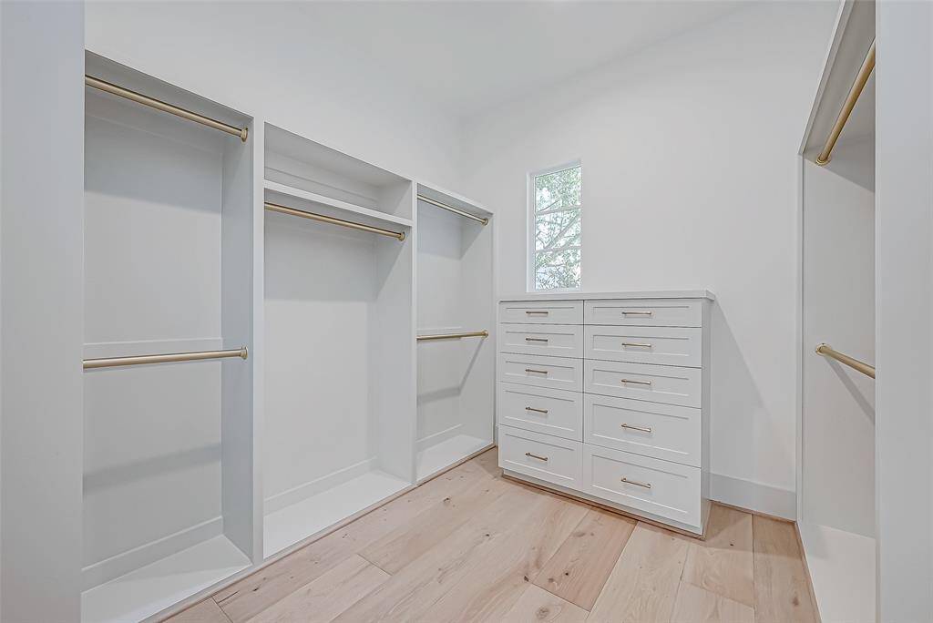 This is a spacious walk-in closet featuring ample hanging space, a window for natural light, and a set of built-in drawers. The light wood flooring and white walls create a bright and airy atmosphere.
