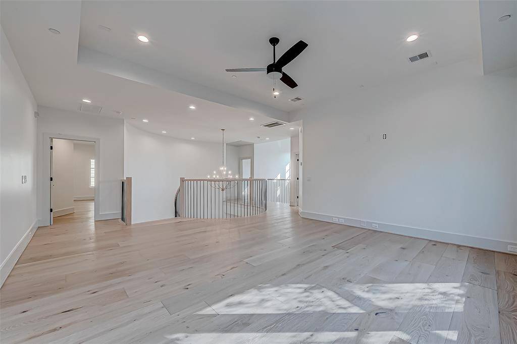 This spacious, light-filled room features elegant wood flooring, recessed lighting, and a modern ceiling fan. It offers an open layout with a view of a stylish staircase, making it ideal for versatile living or entertaining.