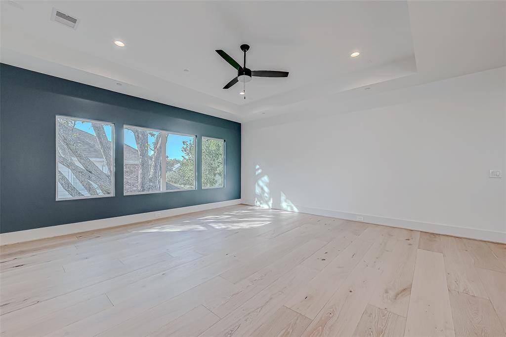 Spacious room with light wood flooring and a dark accent wall. Large windows provide ample natural light, and a ceiling fan adds comfort. Ideal for a modern living space.