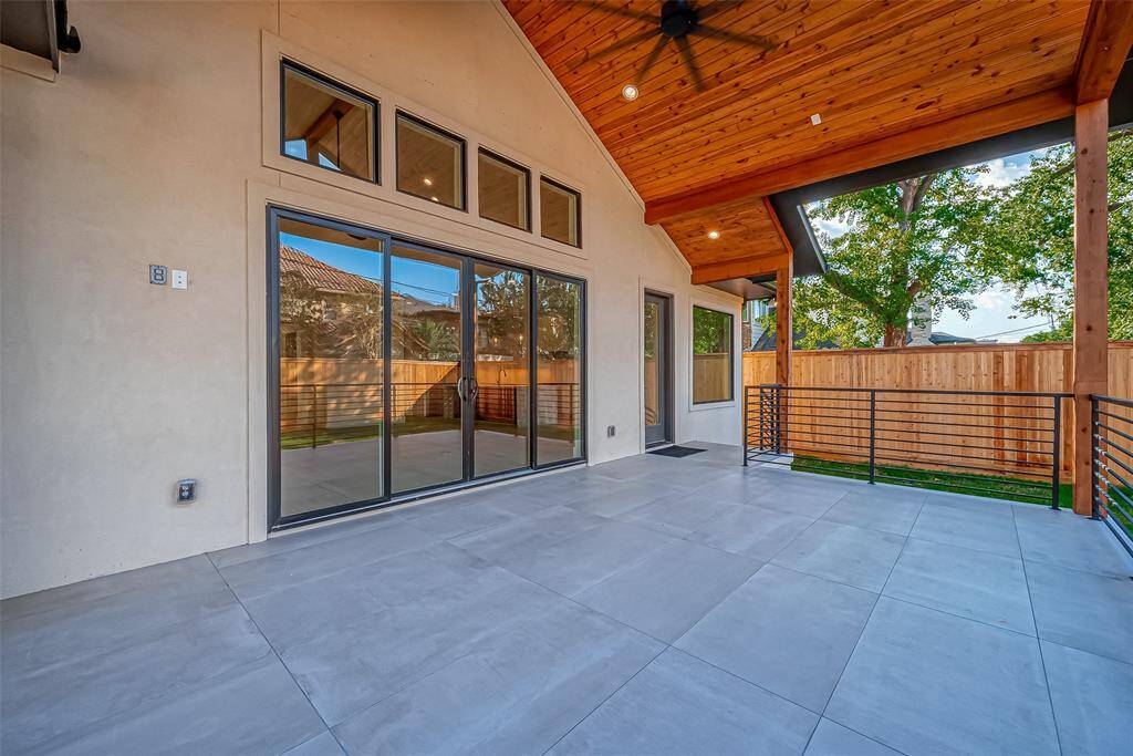 This photo showcases a spacious covered patio with a vaulted wooden ceiling and large sliding glass doors. The area is paved, includes a ceiling fan, and is surrounded by a wooden privacy fence, offering a comfortable outdoor living space.
