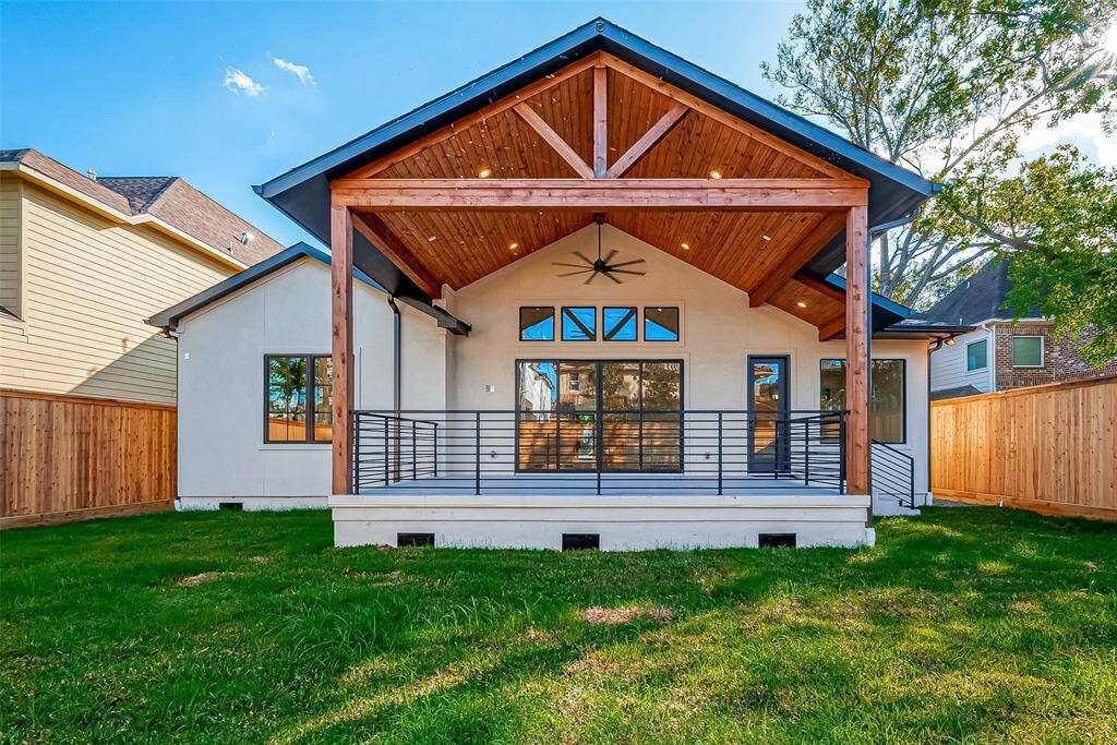Charming modern home with a spacious covered patio featuring wood accents and a ceiling fan. The backyard offers a green lawn, framed by a wooden privacy fence, perfect for outdoor relaxation and entertainment.