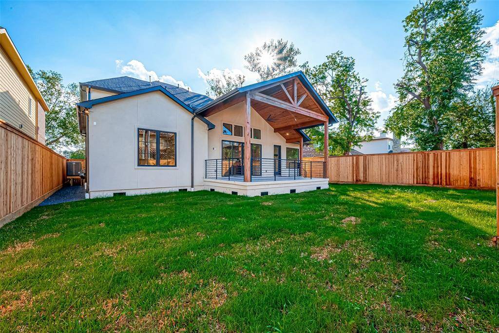 This home features a spacious backyard with a well-maintained lawn, modern architecture, and a covered patio area perfect for outdoor relaxation. It is enclosed by a wooden fence, offering privacy and a cozy feel.