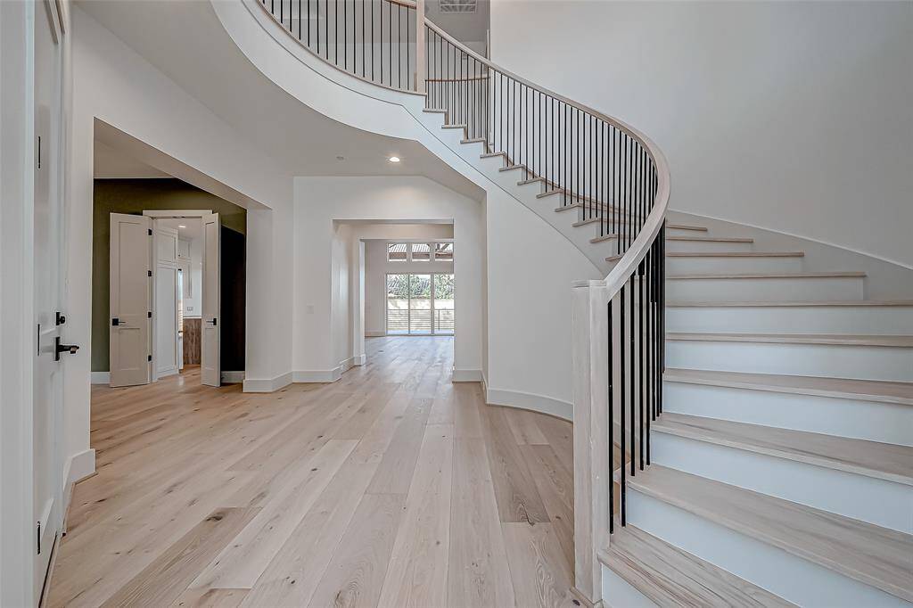 This photo showcases a modern, open-concept entryway with a sweeping curved staircase and light hardwood floors. The space is bright, with high ceilings and a view into a room with large windows.
