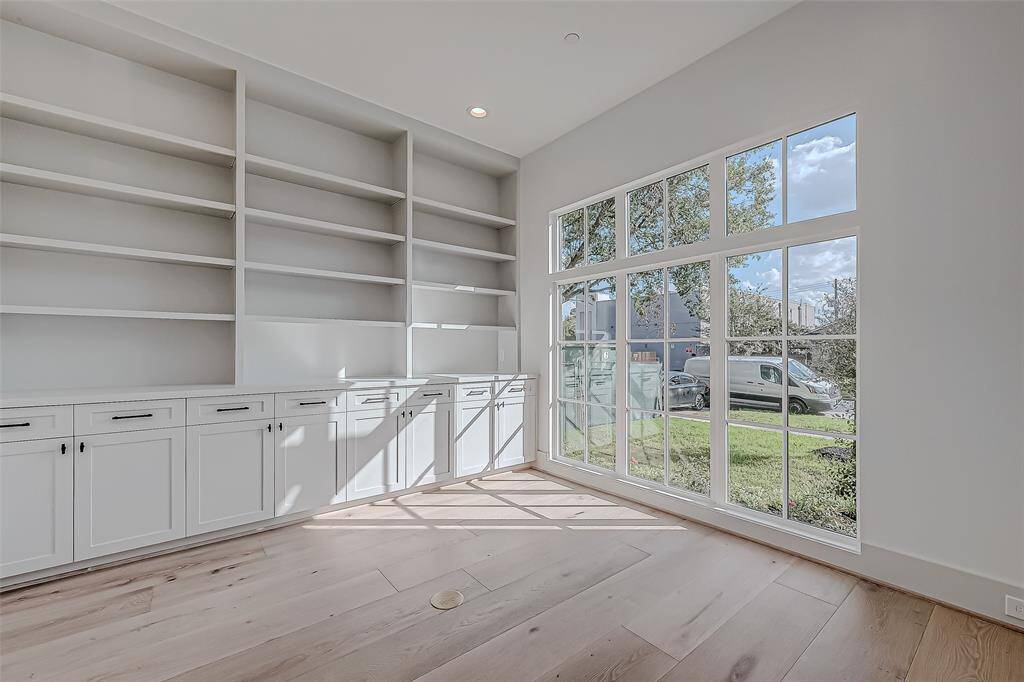 Bright and spacious room with large windows offering plenty of natural light. Features built-in shelves and cabinets for ample storage, and a stylish wooden floor. Ideal for a home office or study.