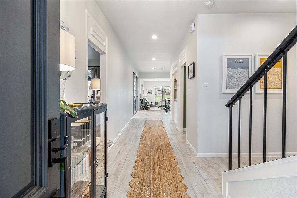 This welcoming entryway features a modern black front door, a staircase with sleek metal railing, light wood effect tile flooring and access to the half bath.