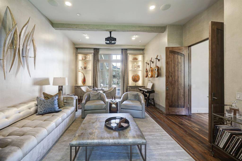 Past the formal living room, enter into a sophisticated music room or study, featuring reclaimed hardwood flooring, 11-foot ceilings, crown molding, and recessed lighting. The room is further adorned with reclaimed wood beams and a projector and drop-down screen.