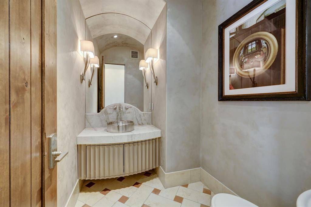The formal powder room is ideally located near the foyer, dining room, and kitchen. It boasts an antique furniture-style vanity with Sea Pearl quartzite countertops, a hammered undermount sink, and brushed nickel fixtures, adding elegance to the space.