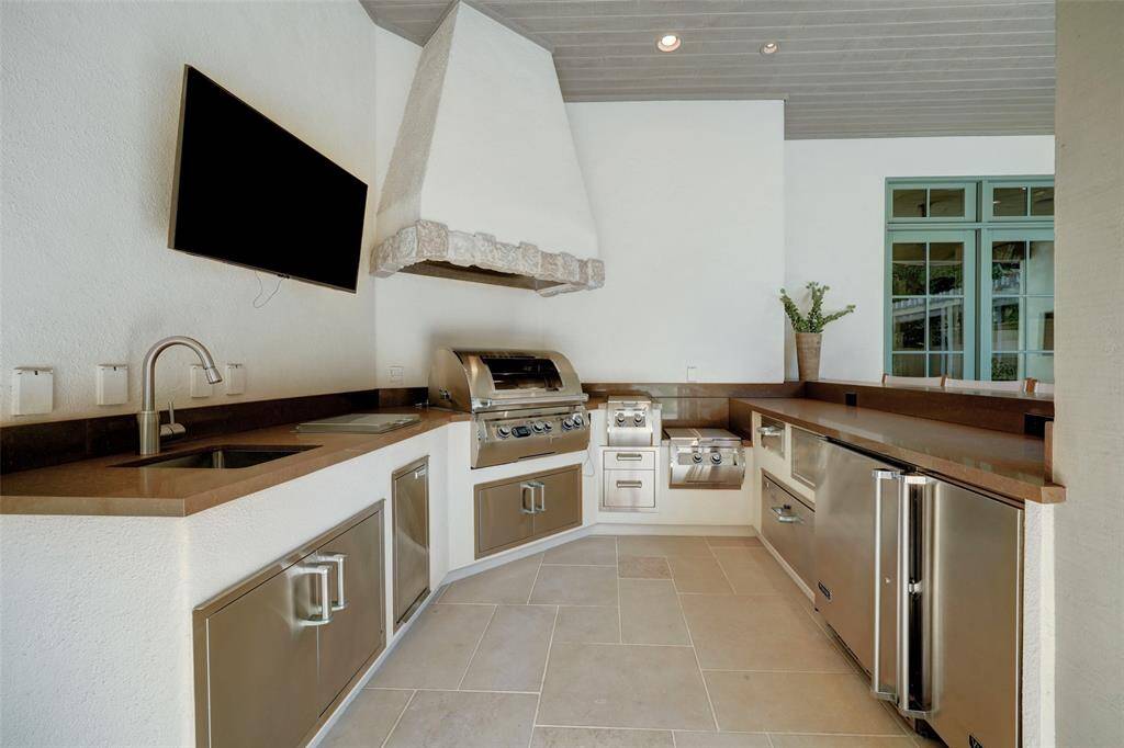 The summer kitchen is an outdoor culinary oasis, featuring top-of-the-line amenities including a DCS stainless steel grill and a U-Line stainless steel beverage chiller.