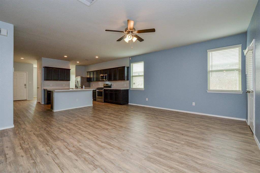 This kitchen features modern dark wood cabinets, stainless steel appliances, and a spacious island with a sink. The open layout and wood-style flooring create a warm, inviting atmosphere.