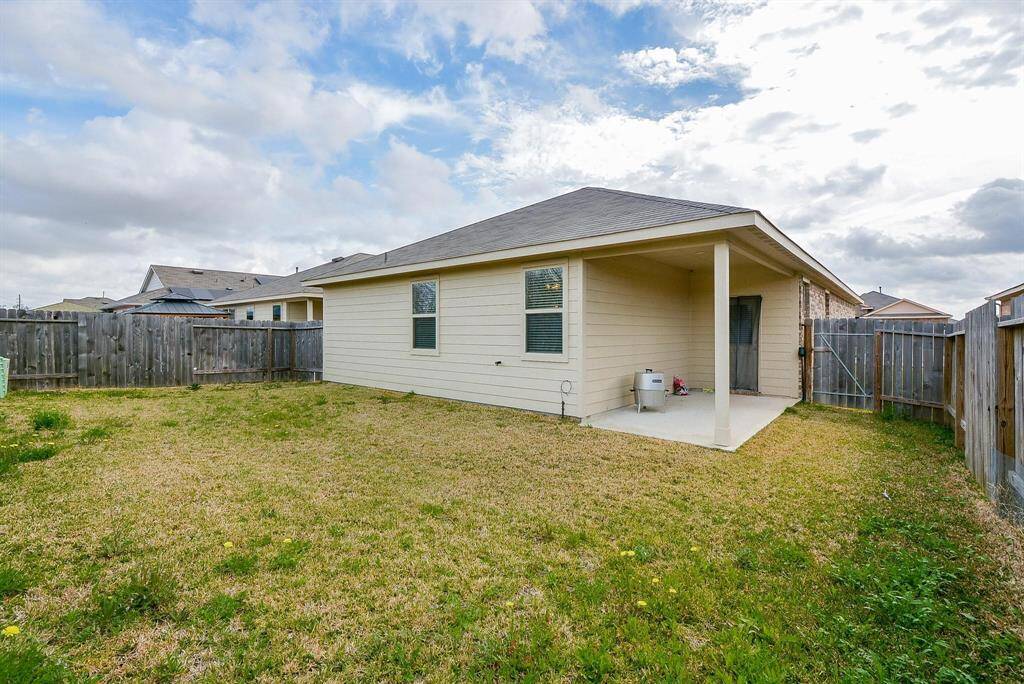 This backyard with a small covered patio attached to a single-story house. The yard has a grassy area, and the home features light-color siding and a sloped roof. It's a simple, private outdoor space ideal for relaxation or small gatherings.