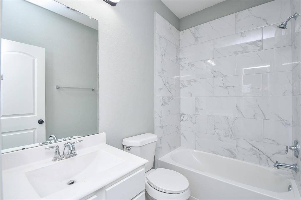 Crisp white cabinetry and a beautifully tiled tub/shower combo give this full bathroom a fresh and polished feel. A well-lit vanity mirror enhances the space, ensuring both function and style.