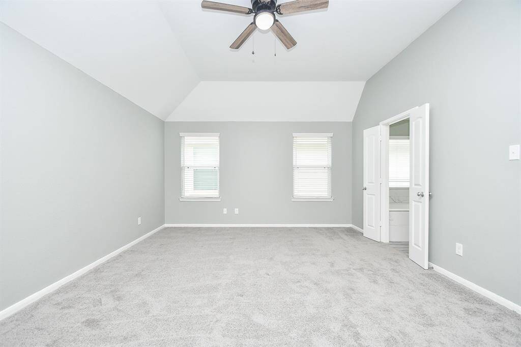 Spacious and bright, the primary bedroom upstairs features soft gray walls, plush carpeting, and gently sloping ceilings that add character. Large windows bring in ample natural light, while a ceiling fan with a light fixture ensures comfort year-round.