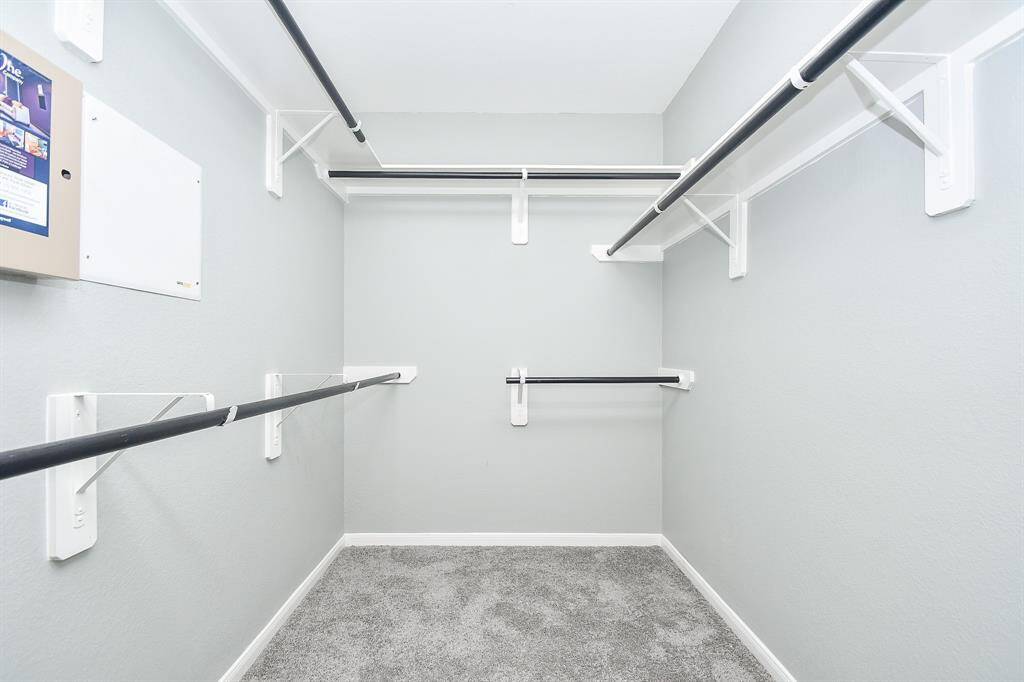 This full entry closet is designed for both storage and organization, featuring built-in overhead shelves for keeping items neatly tucked away. The sturdy hanging racks below provide ample space for coats, jackets, or everyday essentials, all set against a soft carpeted floor.