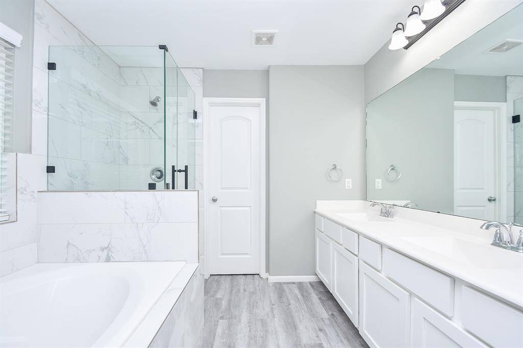 A long vanity with dual sinks and a spacious countertop provides plenty of room for everyday routines. Stylish lighting fixtures and a large mirror enhance the crisp white cabinetry, creating a bright and polished space.