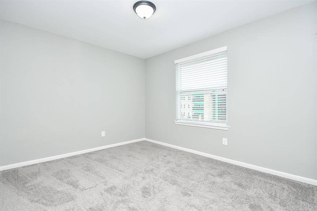 This spacious third bedroom offers soft gray tones, plush carpeting, and a large window for natural light. Its neutral design allows for flexibility.
