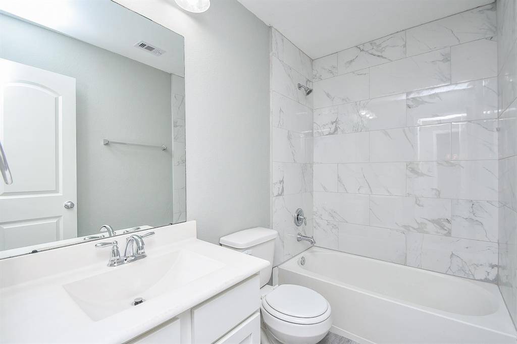 A fresh, modern aesthetic defines this full bathroom, with a bright white vanity, sleek mirror, and tiled tub/shower combination. Thoughtful lighting keeps the space well-illuminated.