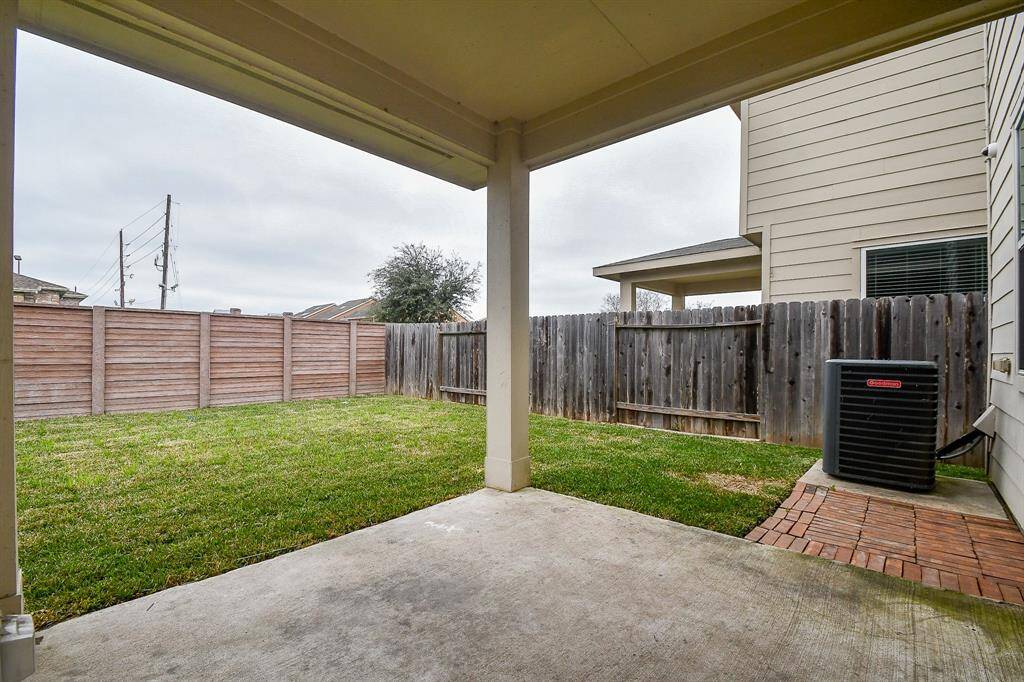 A covered patio extends from the home, offering a shaded space to enjoy the outdoors. The expansive backyard is fully enclosed with a wooden fence, ensuring privacy.