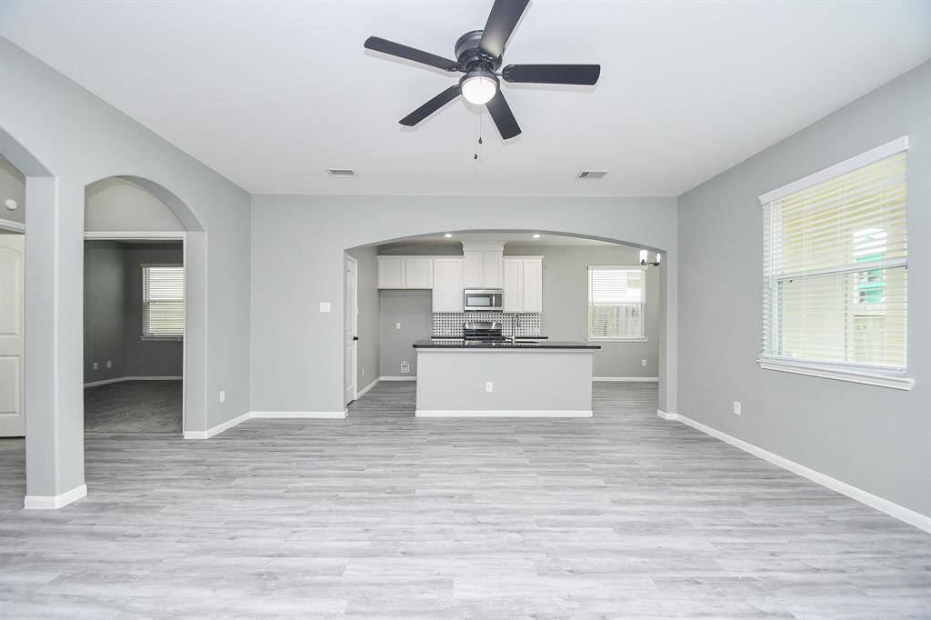 From this view, the living room’s seamless connection to the kitchen becomes clear. A broad archway frames the kitchen entrance, with the island at its center drawing the eye. The open-concept design allows effortless movement between spaces, making this area well-suited for both daily living and entertaining.