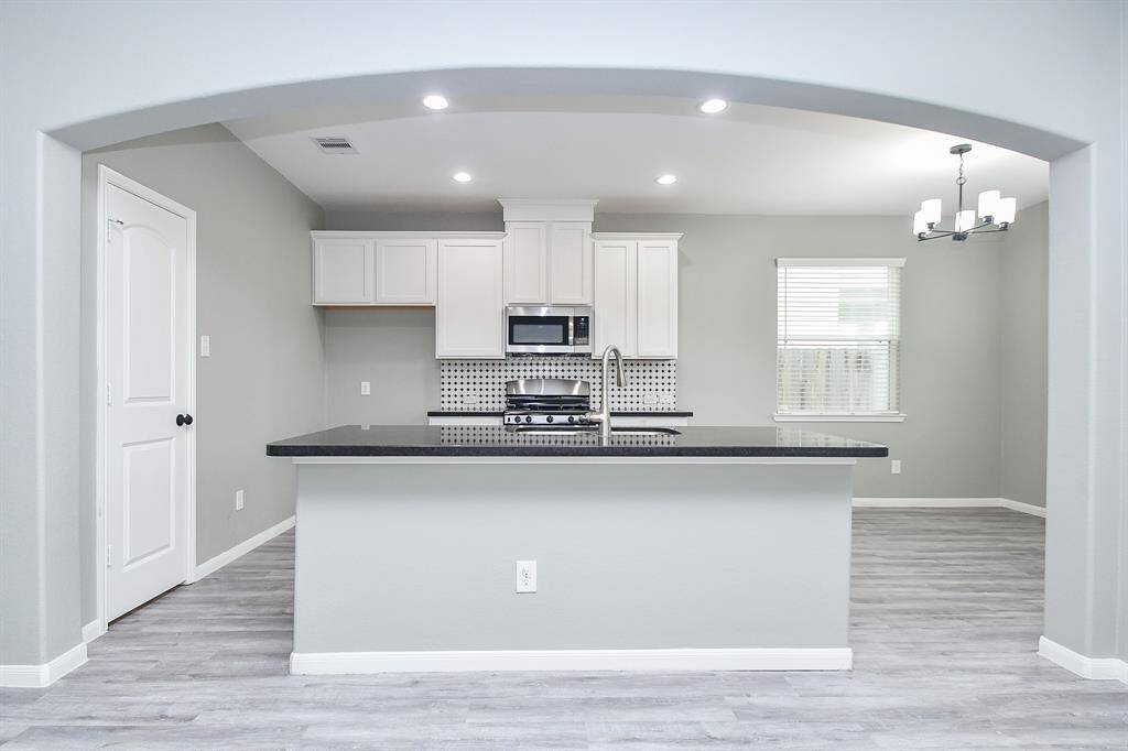 Crisp white cabinetry, black granite countertops, and a striking black-and-white backsplash give the kitchen a bold yet timeless aesthetic. A massive island stands at the center, providing ample space for meal prep, casual dining, or gathering with guests. Recessed lighting keeps the space bright and welcoming.