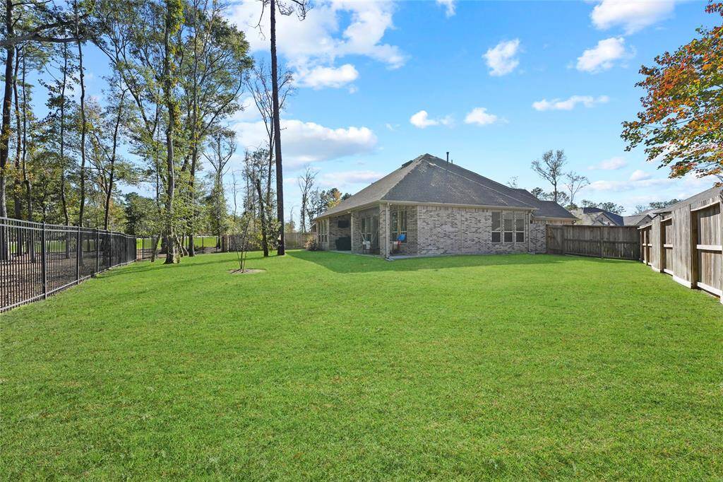 This photo showcases a spacious backyard with a well-maintained lawn, surrounded by a mix of wooden and metal fencing. The brick house has a gabled roof and is set against a backdrop of tall trees, offering a sense of privacy and natural beauty.