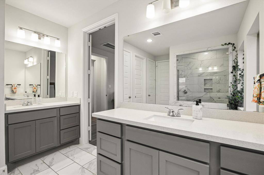 This modern, spa-like primary bathroom features dual sinks with sleek countertops, ample cabinet storage, and large mirrors. The space is well-lit with contemporary fixtures, and a spacious walk-in shower with elegant tile work --adds a touch of luxury. The home has a tankless water heater!