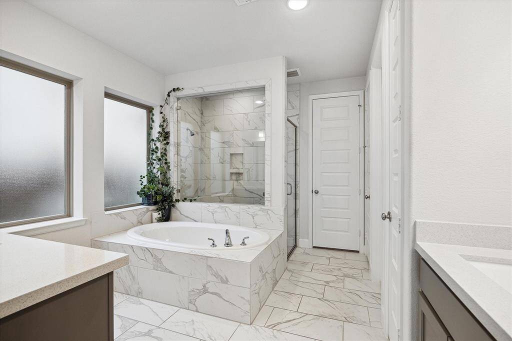 Another view of the gorgeous primary bathroom.  It offers a luxurious soaking tub with marble-style tile, a spacious glass-enclosed shower, and frosted windows for privacy. The neutral tones and sleek design create a modern, relaxing atmosphere.