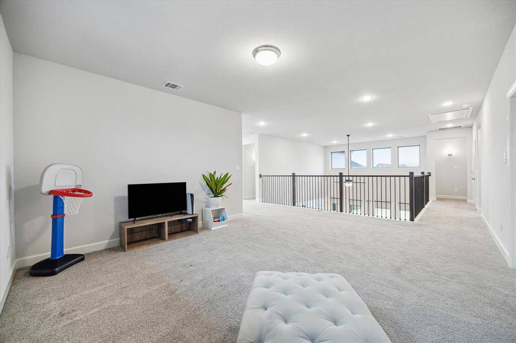 This spacious game room features a cozy carpeted floor, modern lighting, and ample natural light from several windows. It's perfect for a play area with a stylish railing overlooking the main living area.
