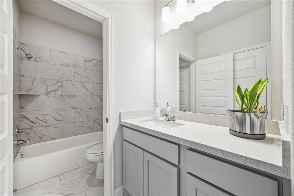 Jack and Jill bathroom featuring a sleek, white vanity with ample storage and a large mirror. The bathtub has elegant marble-style tile.