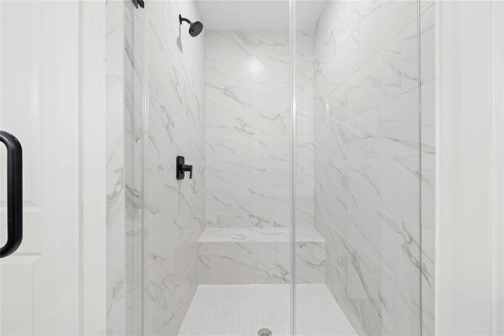 Featuring floor-to-ceiling marble-inspired tile, a sleek glass enclosure, and modern matte black fixtures for a spa-like experience.