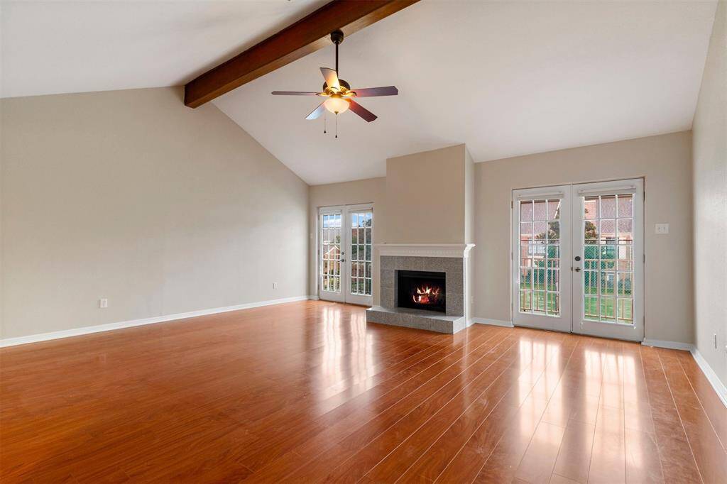 This is a spacious living room with laminate floors, featuring a cozy fireplace and ample natural light from French doors that lead out to a backyard area.