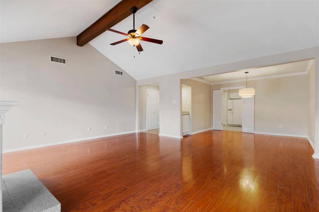 This is a spacious, high vaulted ceilings with exposed beams, and a ceiling fan. The room features a neutral color scheme and offers multiple doorways leading to adjacent spaces, providing a seamless flow throughout the home.